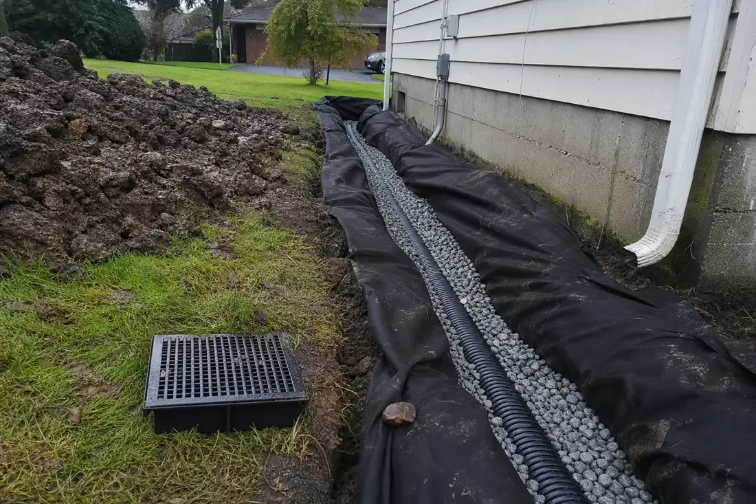 French drain trench with drain rock and perforated pipe along a house in Beaverton, OR