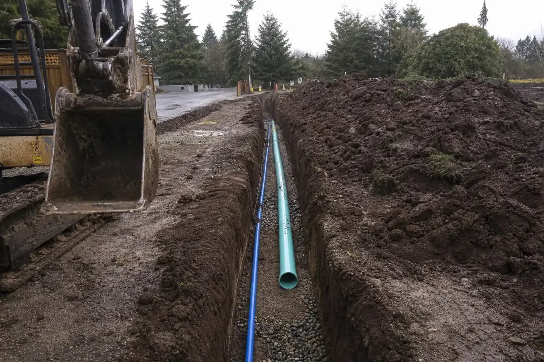 Open utility trench with new water and sewer pipe on gravel bedding in Beaverton, OR